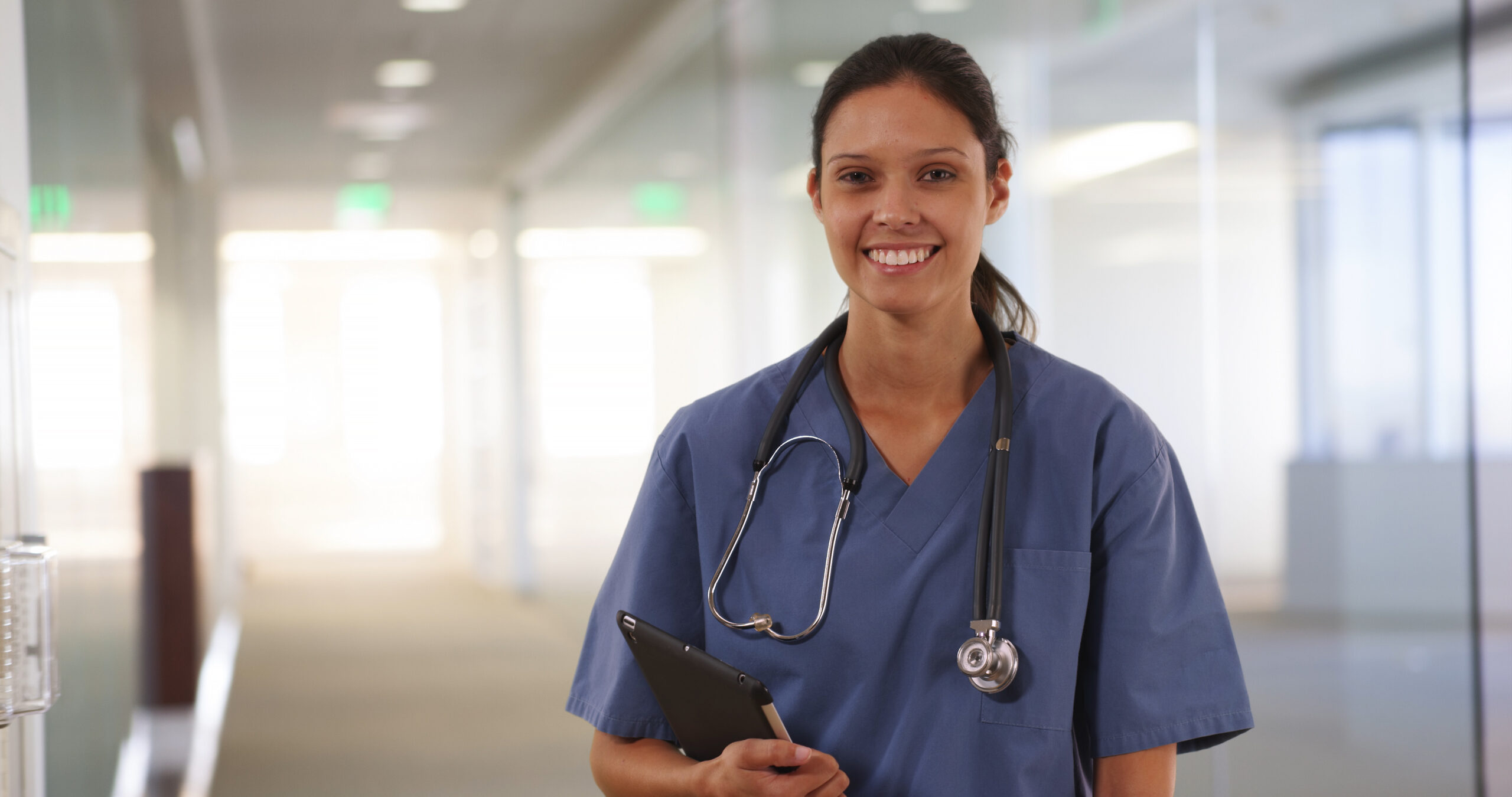 Happy millennial woman nurse or doctor smiling at camera in hallway