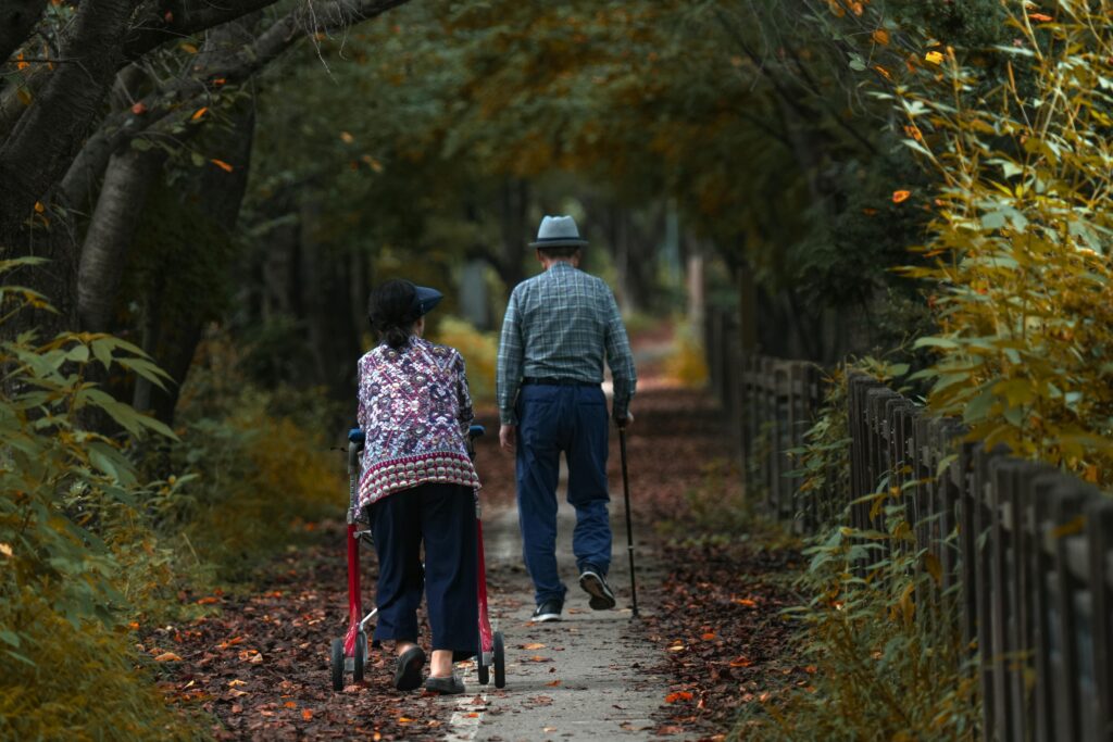 pexels-photo-18149636-18149636 Asian elderly couple strolling through a serene autumn forest path, enjoying nature's beauty.